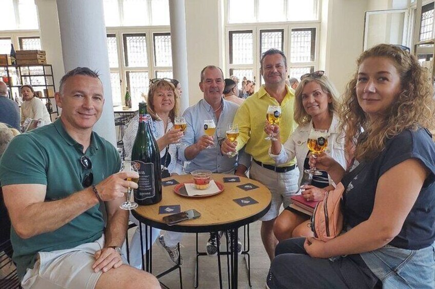 A group of people sitting around a table, holding glasses of beer and a bottle of wine. 2