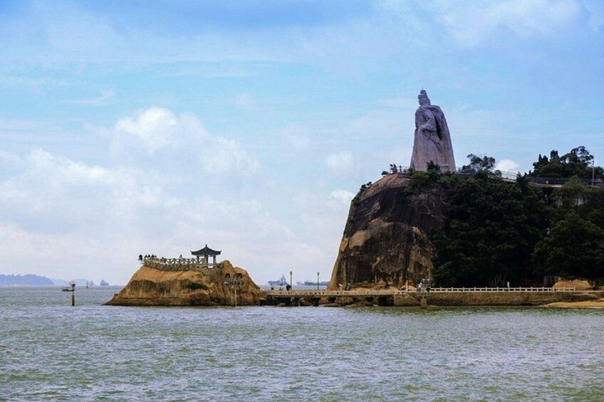 A large rock formation with a statue on top, a smaller rock with a pavilion, and a body of water in the foreground. 1