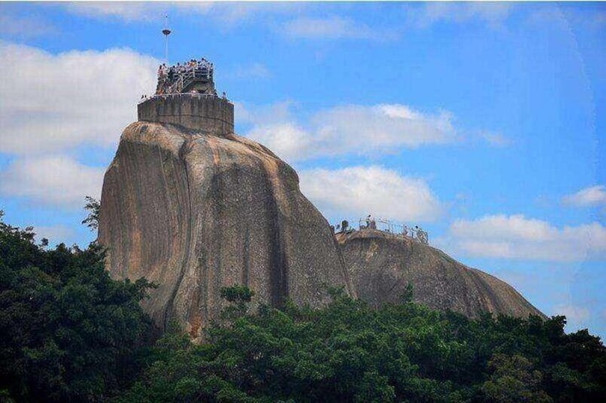A large rock formation with a statue on top, surrounded by dense greenery. 2