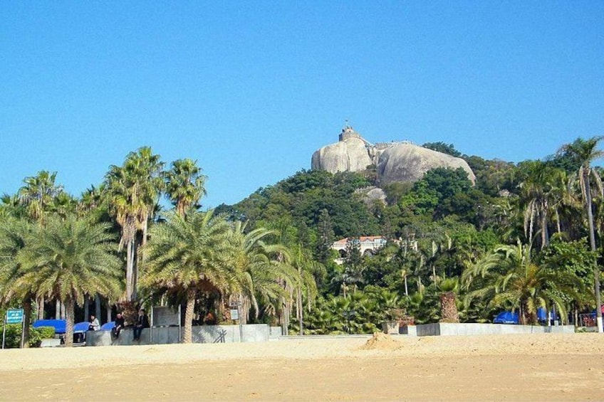 A beach with palm trees, a large rock formation, and a building in the background. 3