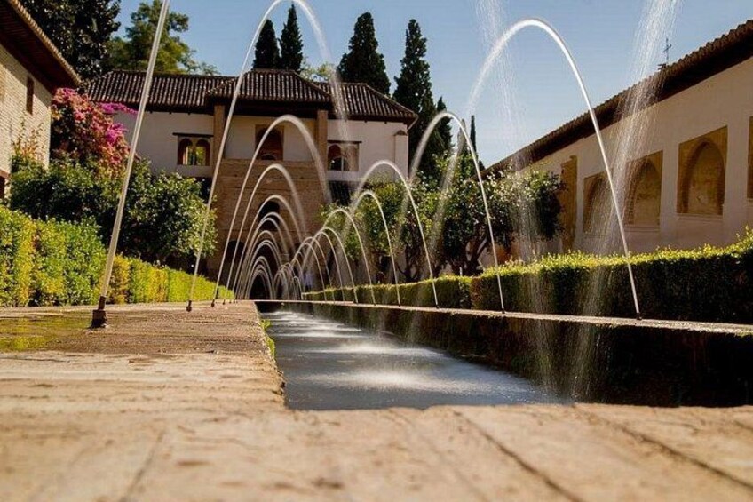 Ein Brunnen mit Wasserspielen in einem Innenhof, im Hintergrund ein Gebäude. 2