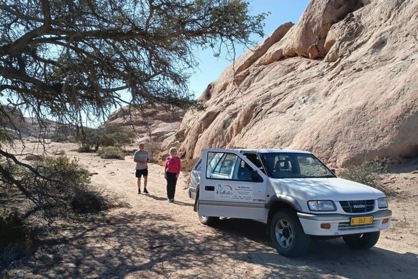 A white SUV parked on a dirt path with two people walking away from it. 3