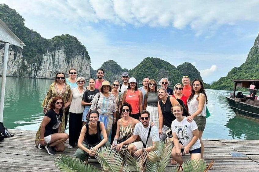 A group of people on a wooden dock by a body of water with cliffs in the background. 2