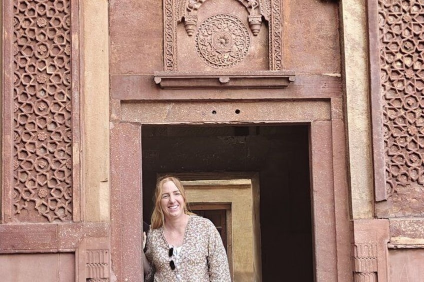 A person standing in front of a doorway with intricate carvings and a circular emblem above it. 4