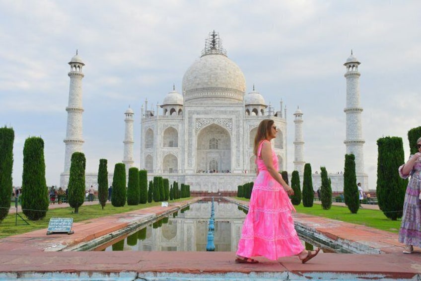 The Taj Mahal with a person in a pink dress walking in the foreground. 1