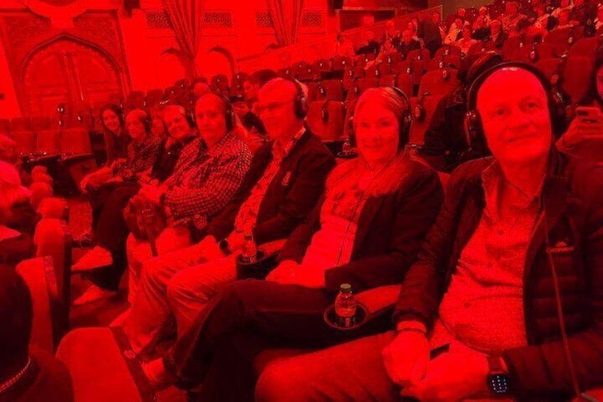 A group of people seated in a dimly lit room with red lighting. 2