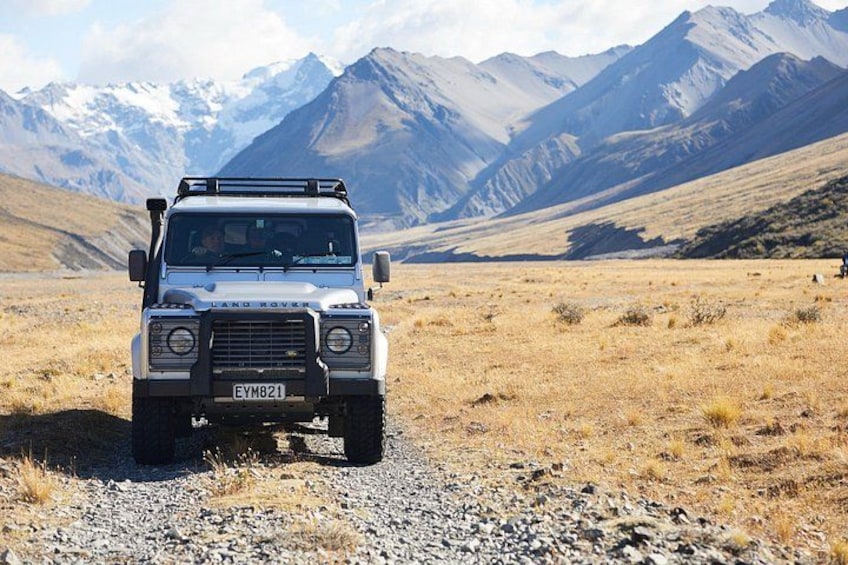 En Land Rover i et tørt, bjergrigt landskab med sneklædte bjergtoppe i baggrunden. 3