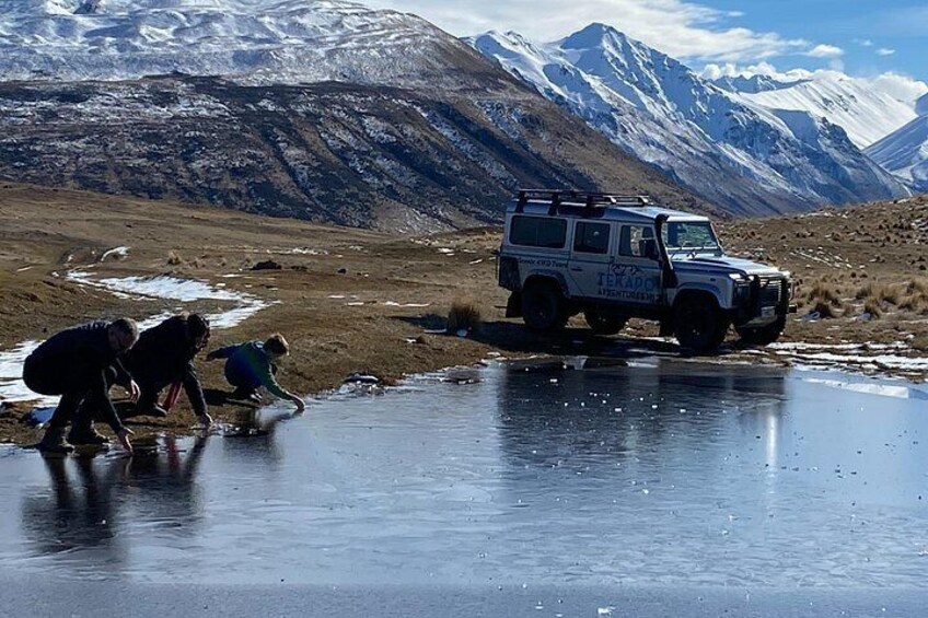 A group of people collecting water from a frozen stream, a vehicle labeled 'TERADOK,' and snow-capped mountains in the background. 3