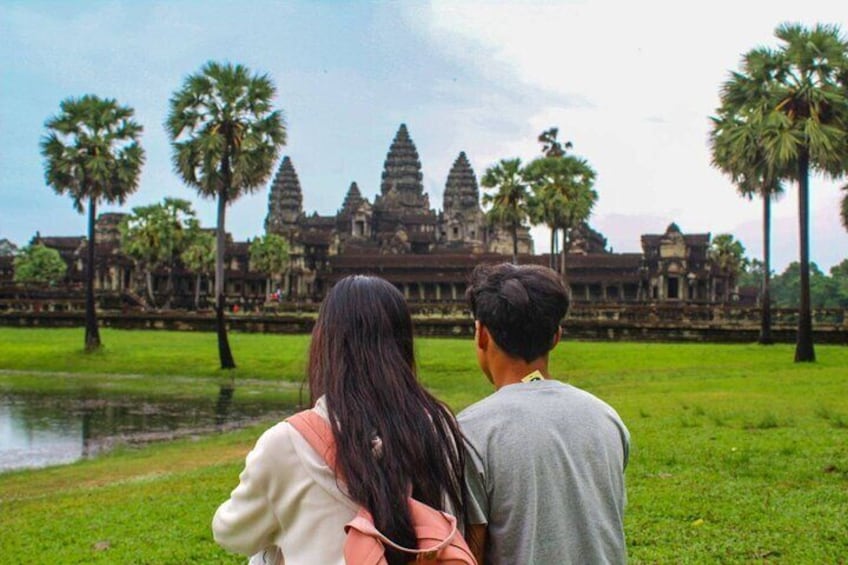A couple standing in a grassy area with a temple in the background. 4