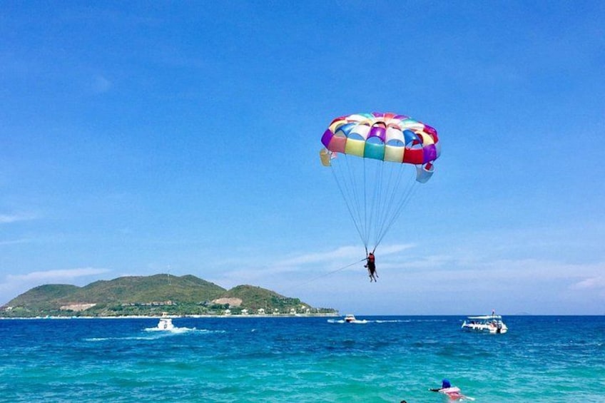 Une personne pratiquant le parachutisme avec un parachute multicolore au-dessus d’une étendue d’eau où se trouvent des bateaux et une île au loin. 1