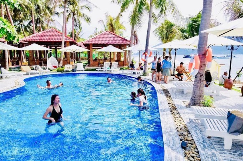 Une piscine où l’on voit des personnes dans l’eau, entourée de chaises longues et de parasols. 2