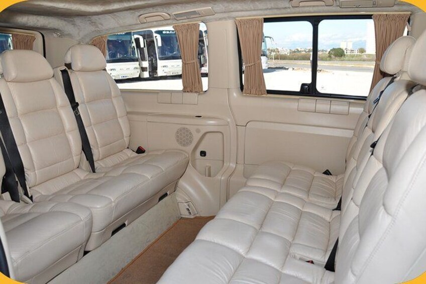 A vehicle interior with beige leather seats, a central aisle, and windows with curtains. 2