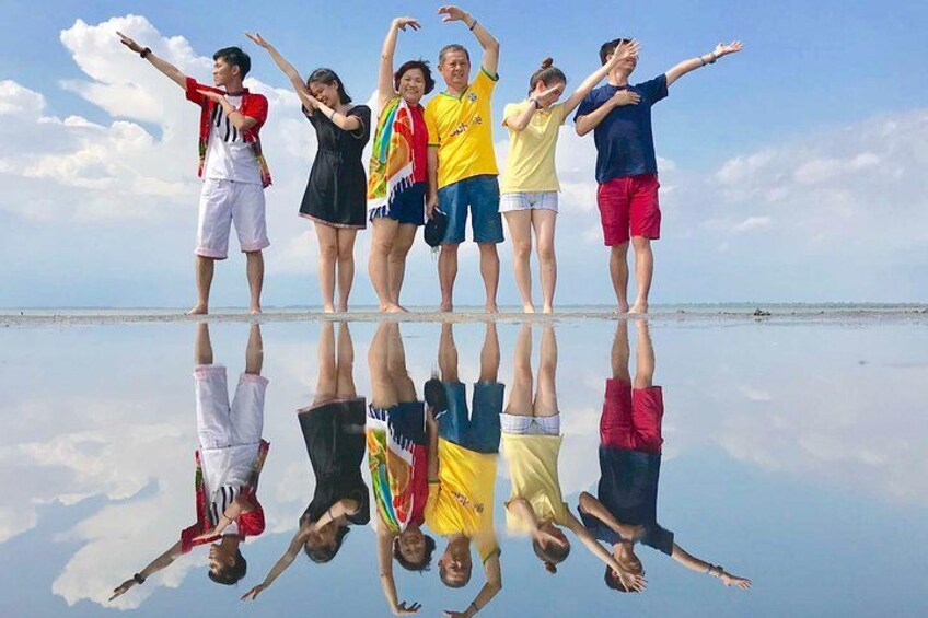 A group of people standing on a reflective surface with their arms raised, reflecting their poses. 1