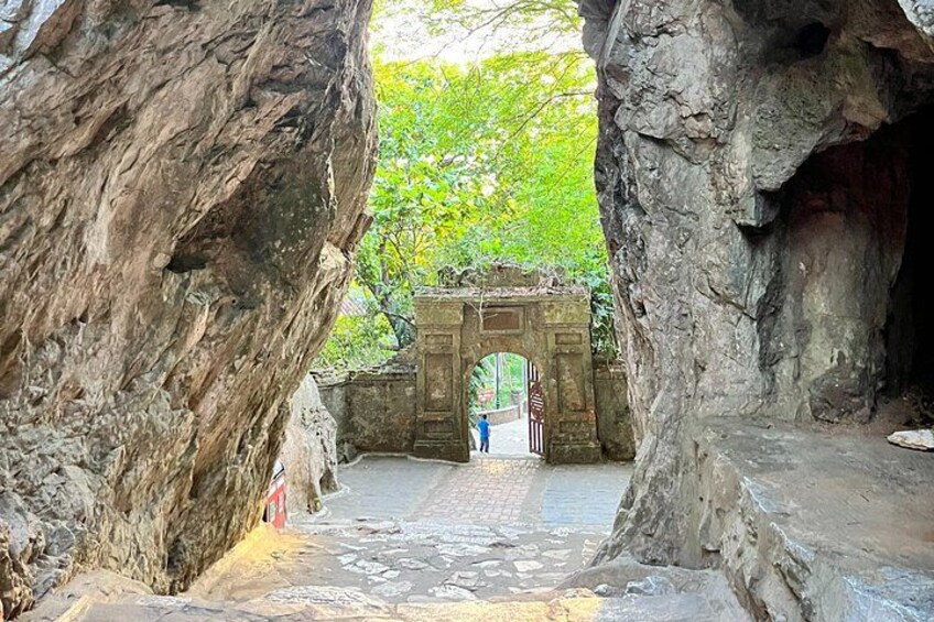 A cave entrance with a stone archway, a paved path, and a person standing in the distance. 3