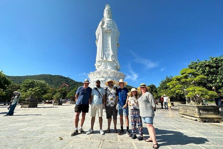 A group of people posing in front of a large white statue in a plaza with trees and a clear sky. 2