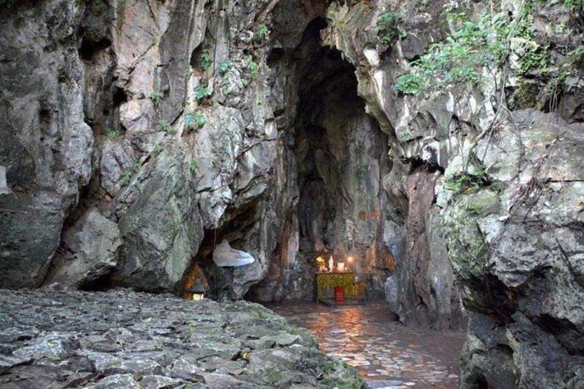 A cave entrance with a small pool of water, rocky walls, and a candle-lit altar. 4