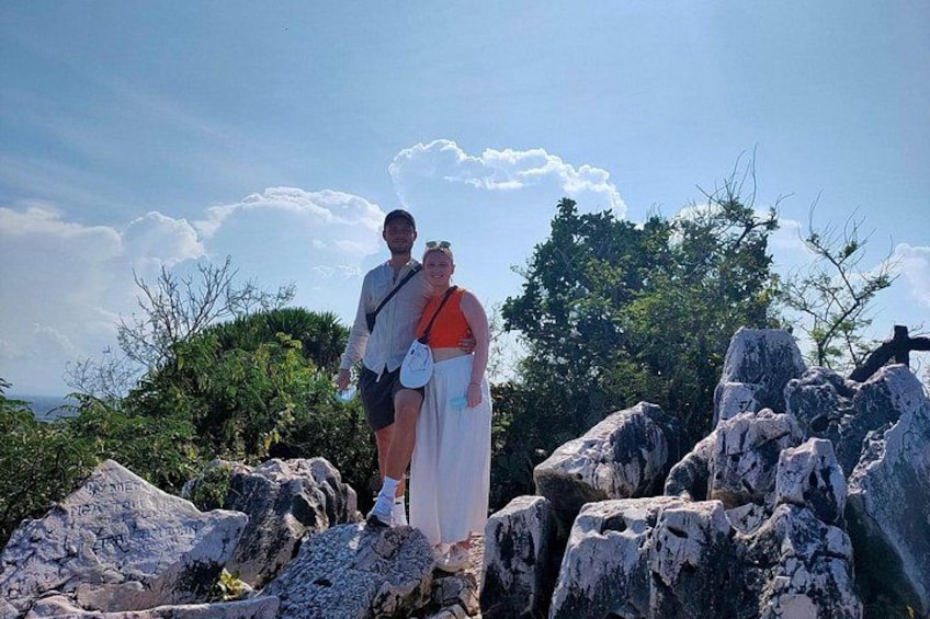 A couple standing on rocky terrain with a cross and trees in the background. 2