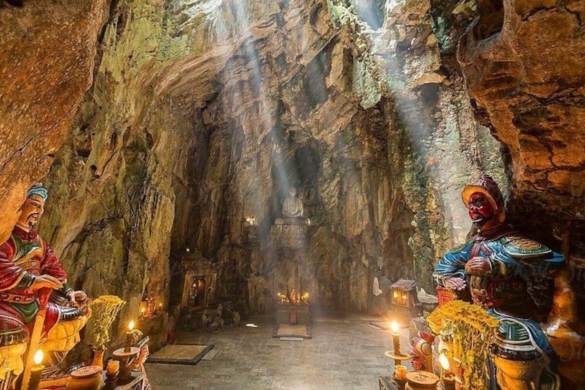 A cave interior with two figures in colorful attire, a central altar, and various ritual items. 5