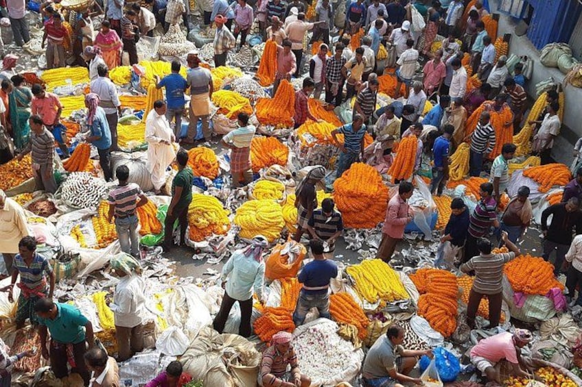 Een drukke markt met mensen die waren aanbieden en kopen, voornamelijk oranje en gele stoffen. 5