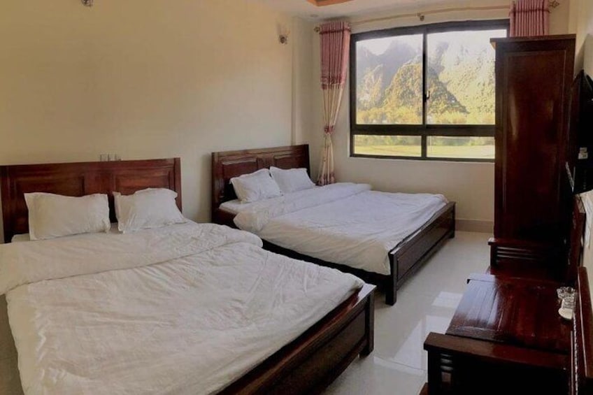 A hotel room with two wooden beds, a wooden wardrobe, and a window with curtains. 2