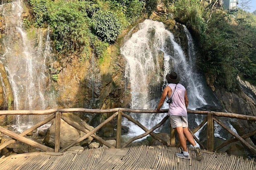 A person standing on a wooden bridge overlooking a waterfall. 2