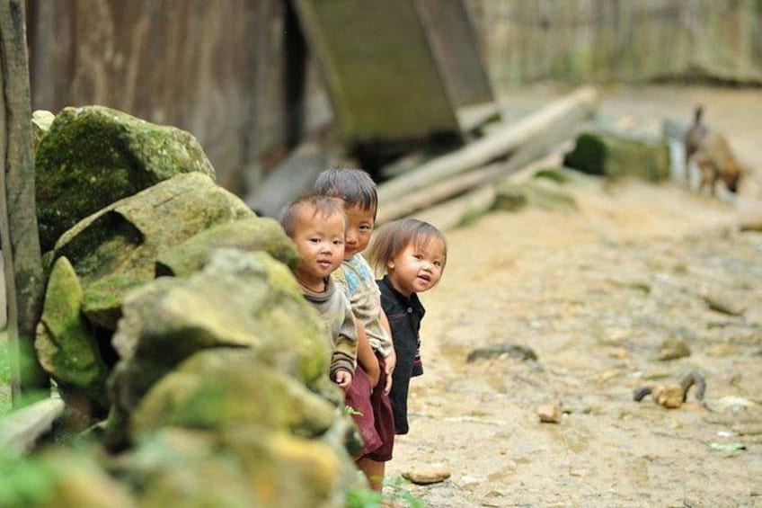 Children standing near a rocky area with a wooden structure in the background. 2