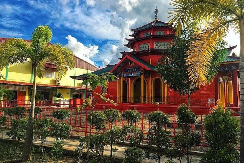 A traditional multi-tiered temple with red and yellow walls, surrounded by a fence and palm trees. 3
