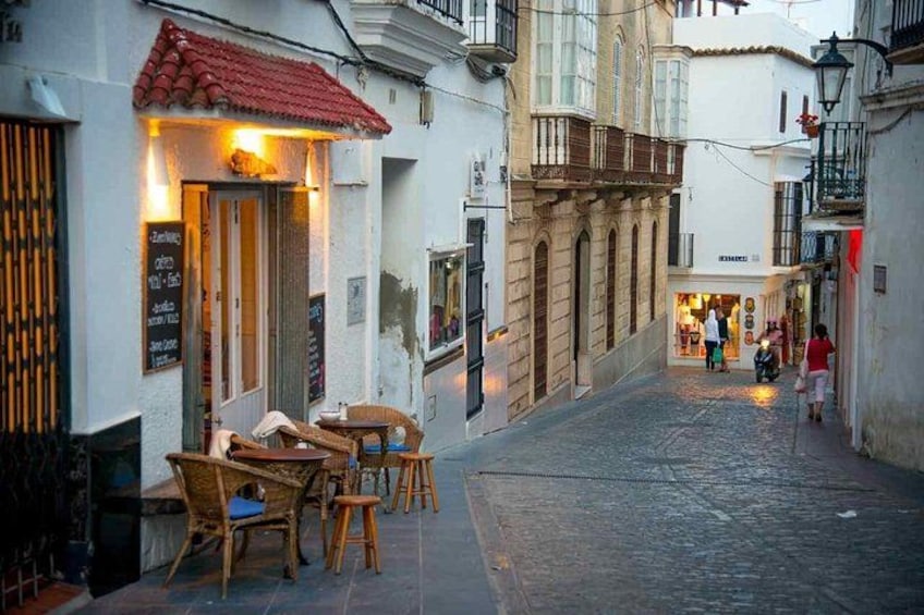 A narrow street with outdoor seating, a café, and a shop in the background. 5