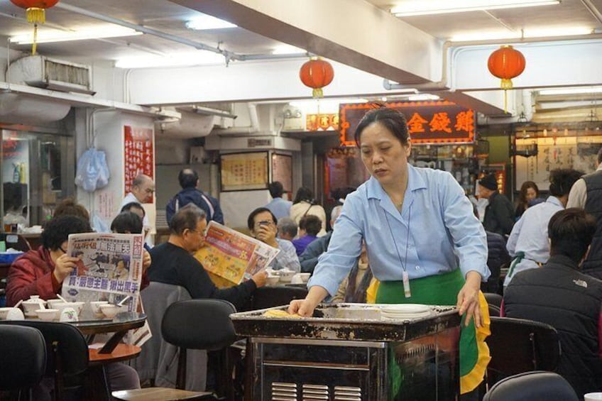 Un marché intérieur animé, où l’on peut voir des gens assis à des tables, un vendeur qui sert de la nourriture et des décorations traditionnelles. 4
