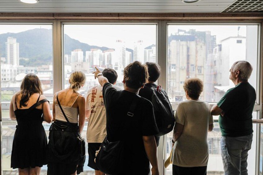 Un groupe de personnes se tient près d’une grande fenêtre, d’où l’on peut admirer un paysage urbain avec de hauts immeubles et une montagne à l’horizon. 4