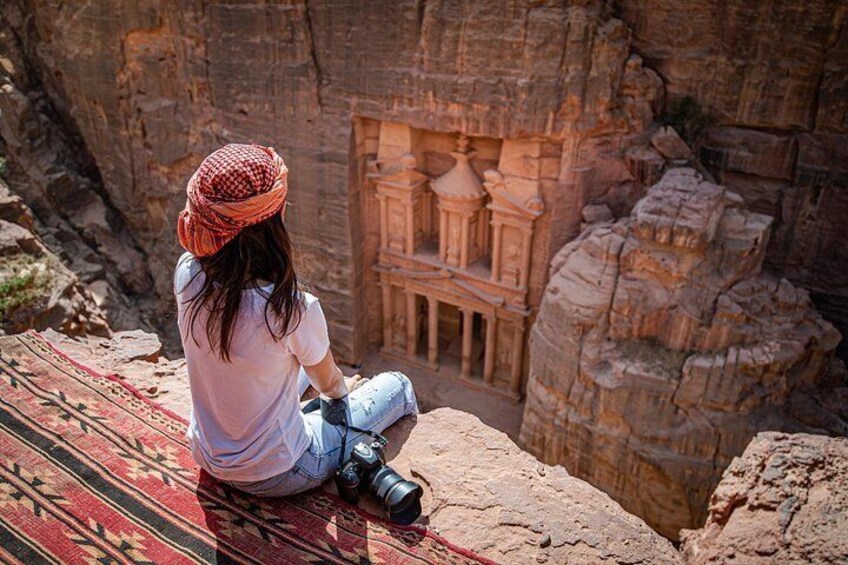 A person sitting on a patterned rug, looking at a carved rock structure. 3