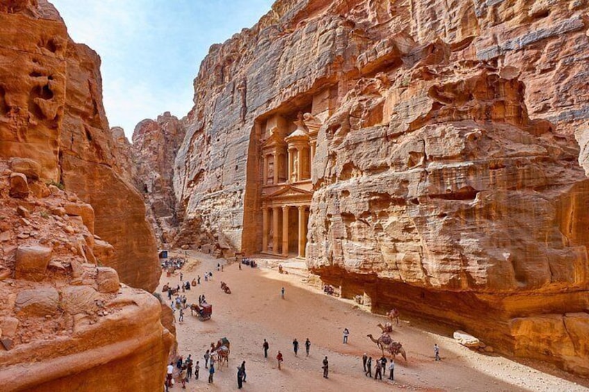 A historic rock-cut city with a large building, narrow passageways, and people walking. 5