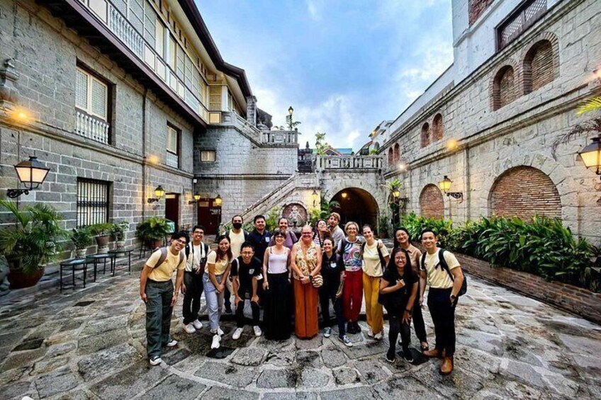 A group of people standing in a courtyard with stone buildings, a bridge, and potted plants. 5
