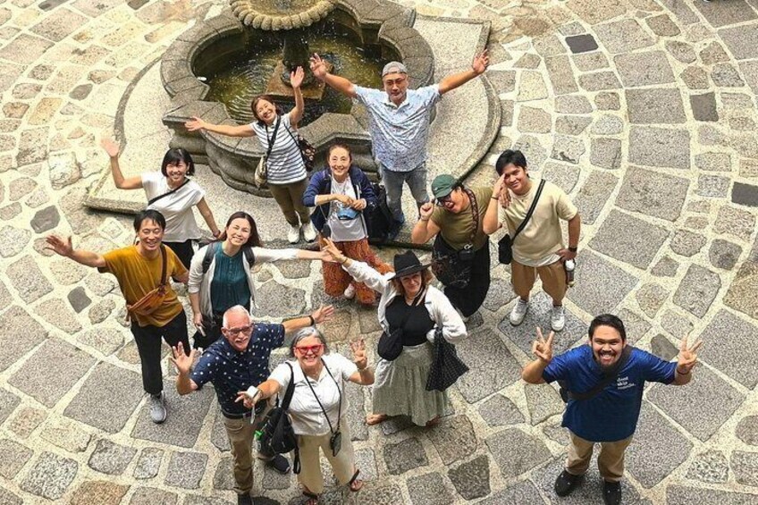 A group of people standing in a circular stone plaza with a fountain in the center. 2