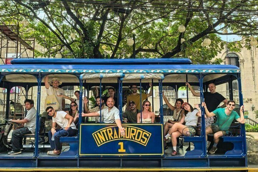 A group of people on a blue trolley labeled 'INTRANAMROOS 1' with a tree-lined street in the background. 3
