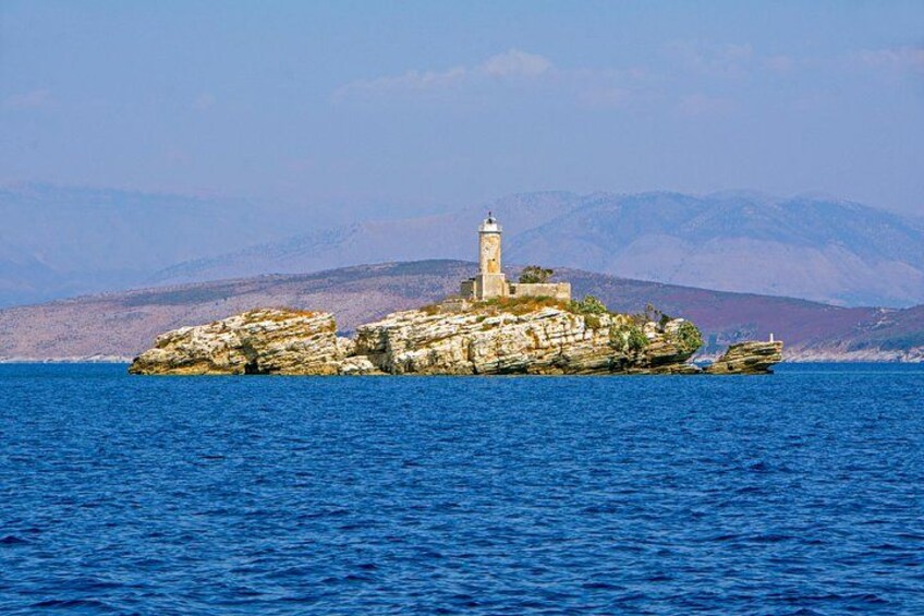 A rocky island with a lighthouse in the sea, surrounded by mountains. 4