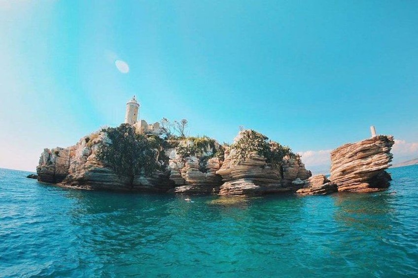 A rocky island with a lighthouse and clear blue waters. 2