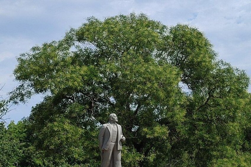 A statue of a man in a suit standing in front of a large tree. 4
