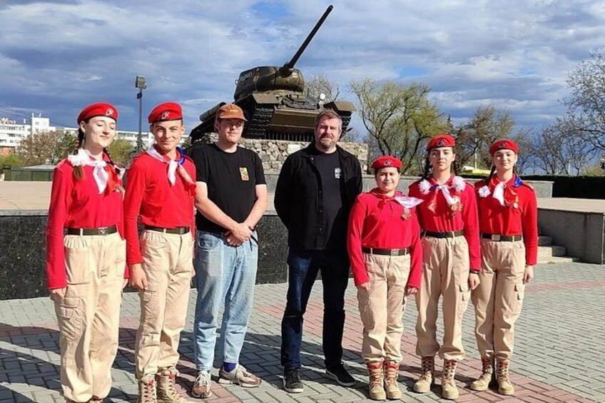 A group of people in red uniforms standing in front of a tank. 2