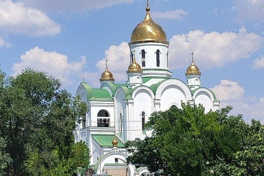 A white church with green domes and gold accents, surrounded by trees. 3