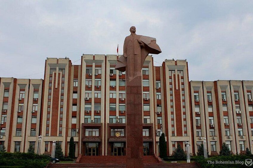 A large statue in front of a multi-story building with a red and white facade. 1