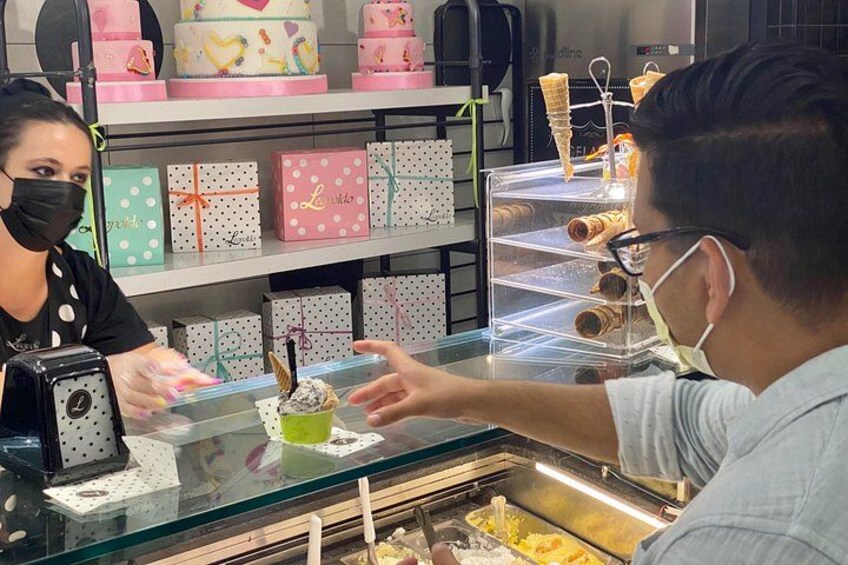 A bakery counter with a customer and a server. There are decorated cakes and pastries on display. 2
