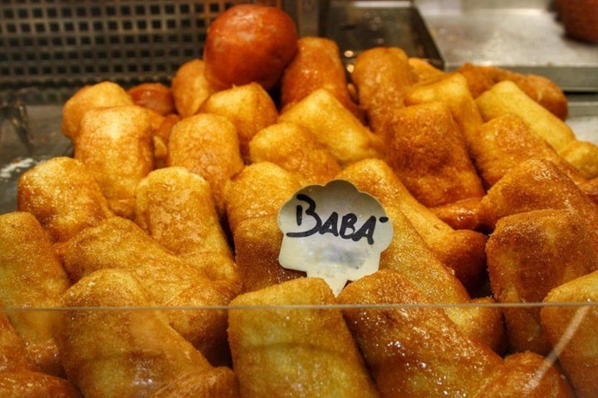 A display of golden-brown fried items, likely fritters, with a sign reading 'BABA'. 3
