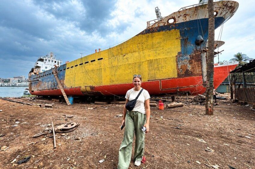 Una persona in piedi di fronte a una grande nave relitta arrugginita su una spiaggia sabbiosa. 2