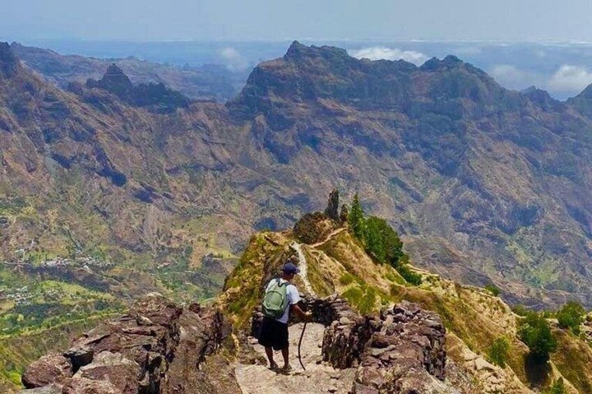 A hiker on a mountain trail with rugged terrain and distant valleys. 3