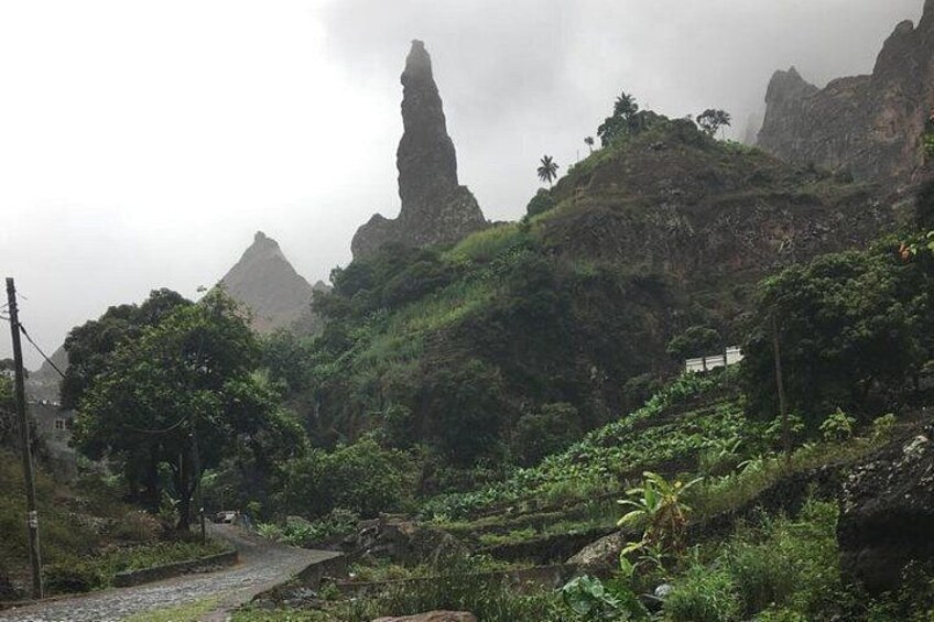 A mountainous landscape with a narrow path, lush greenery, and a prominent rock formation. 4