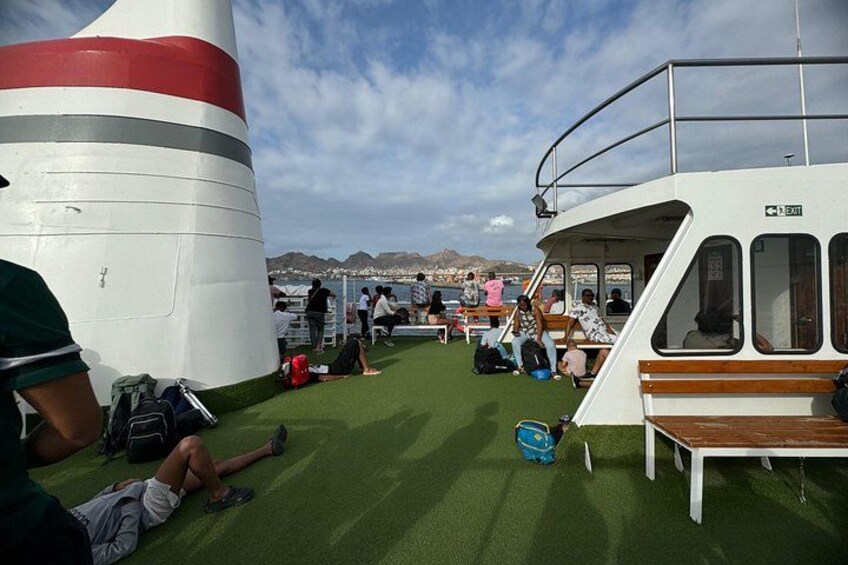 A boat with people sitting on the deck, a grassy area, and a mountainous landscape in the background. 2
