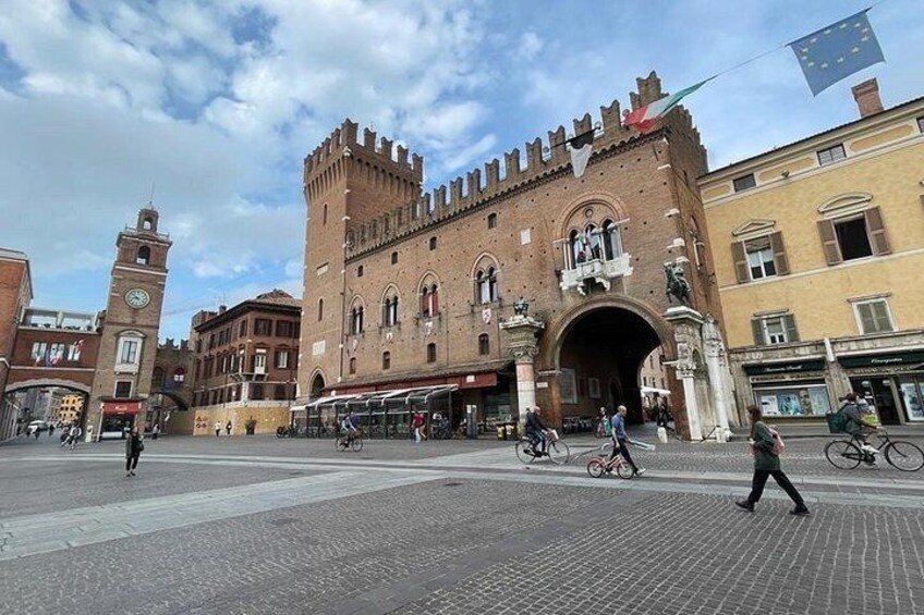 A historic building with a clock tower, a large archway, and a flag. 3