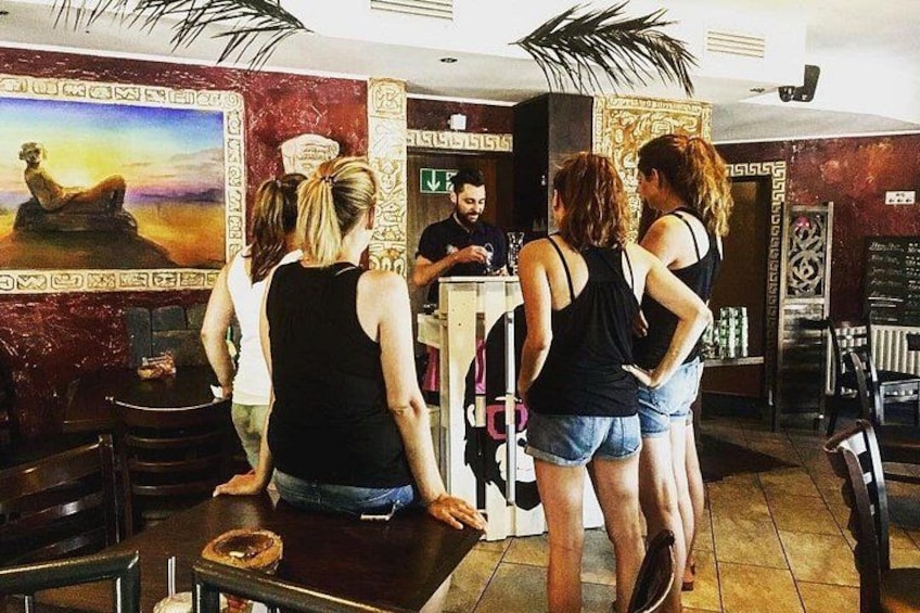 A group of people standing at a bar counter in a restaurant with a mural and decorative columns. 5