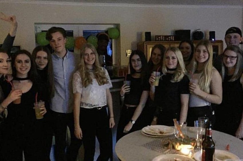 A group of people at a dinner table with a lit candle, surrounded by balloons and a clock on the wall. 3